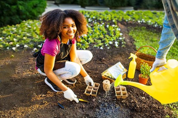 beautiful young woman with afro hairstyle working at her garden at sunset spring time outdoors.